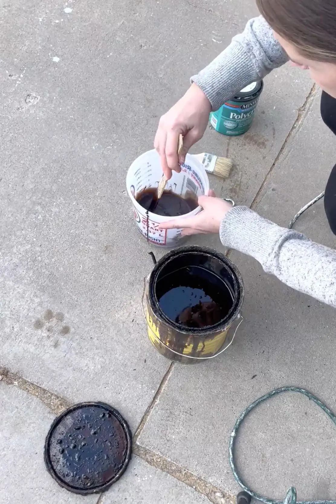 A DIYer tests the color of a dark wood stain by dipping a stir stick into the mixture before applying it.